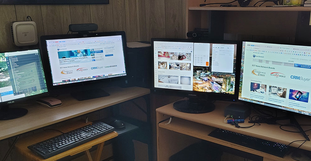 Four-monitor dual-desk home office setup powered by mini-PCs, displaying web browsers and productivity tools.